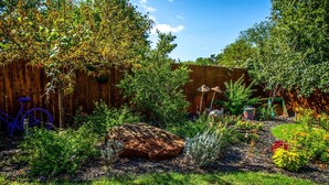 A garden with a wooden fence, a bicycle, and various plants and flowers.