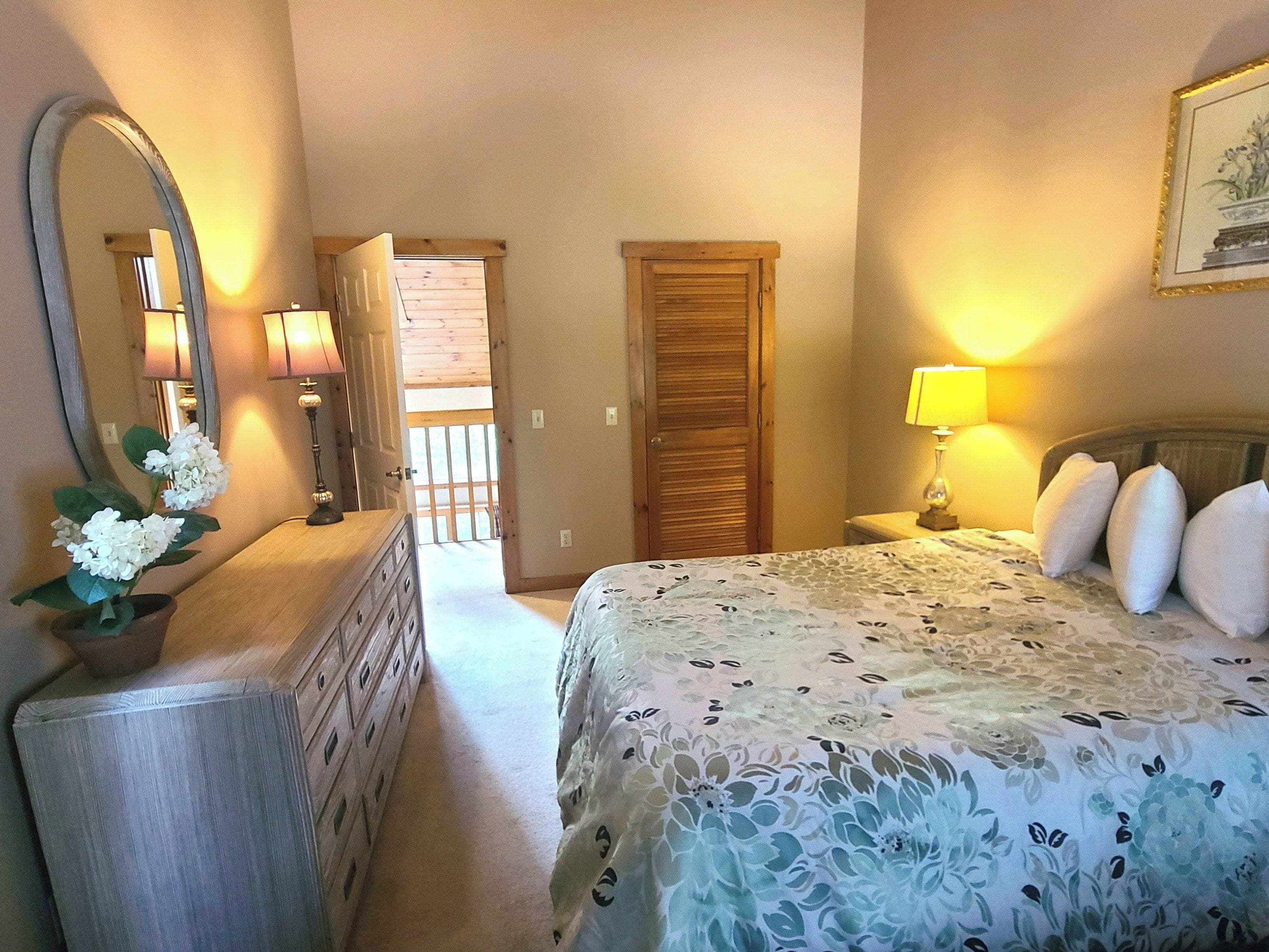 A bedroom with a bed, dresser, mirror, and bedside lamps.