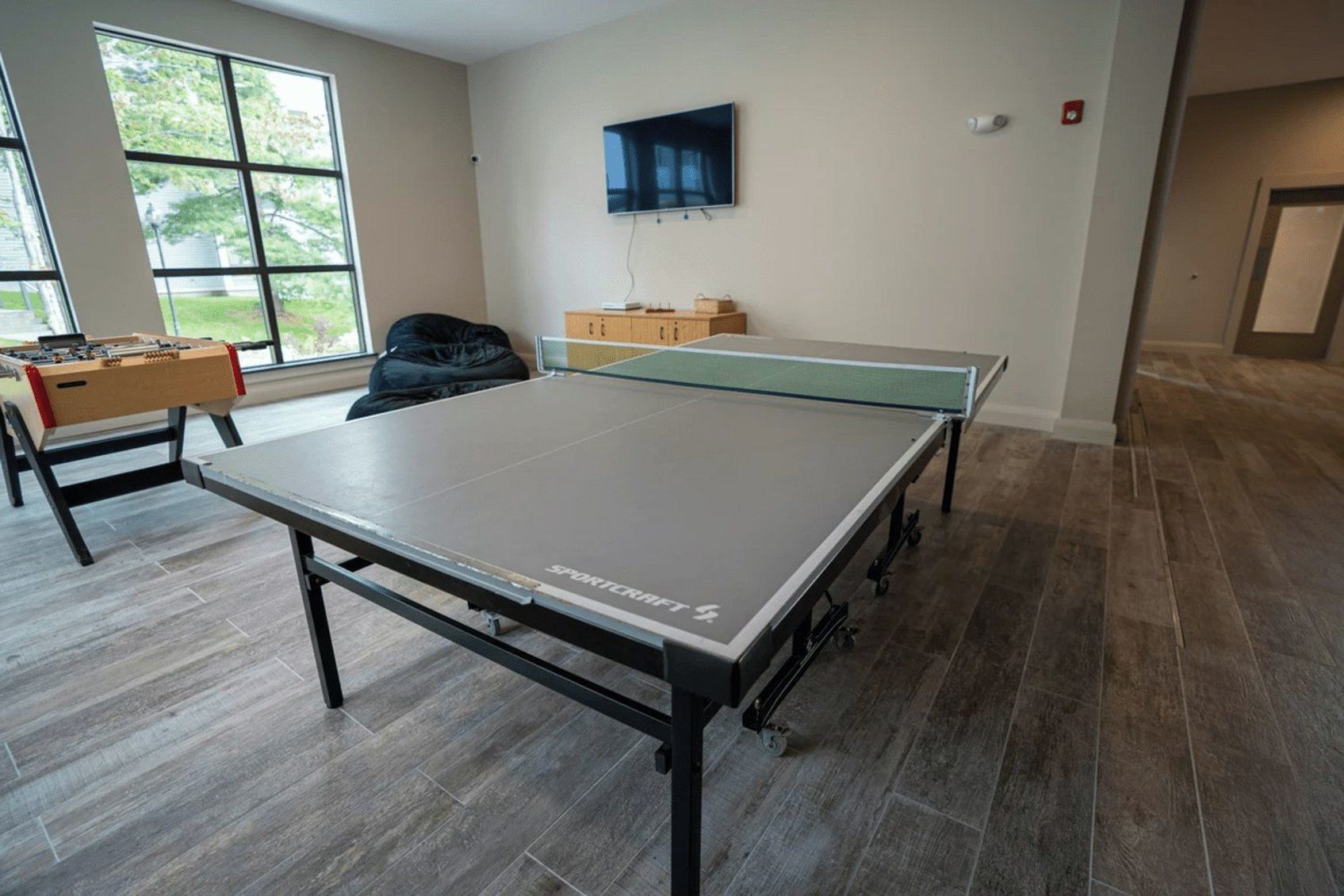 A room with a ping pong table, a foosball table, and a TV mounted on the wall.
