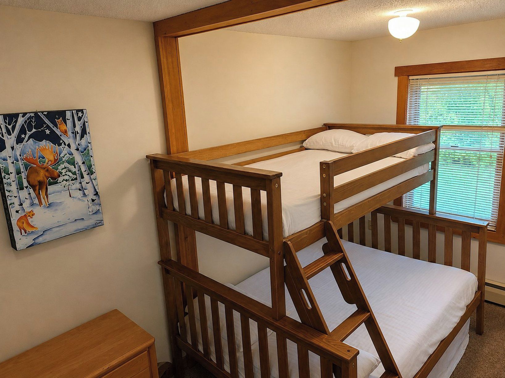 A bunk bed with a wooden frame, a bedside table, and a painting on the wall.
