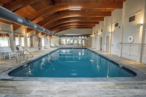 Una piscina interior con suelo de piedra, vigas de madera en el techo y paredes blancas.