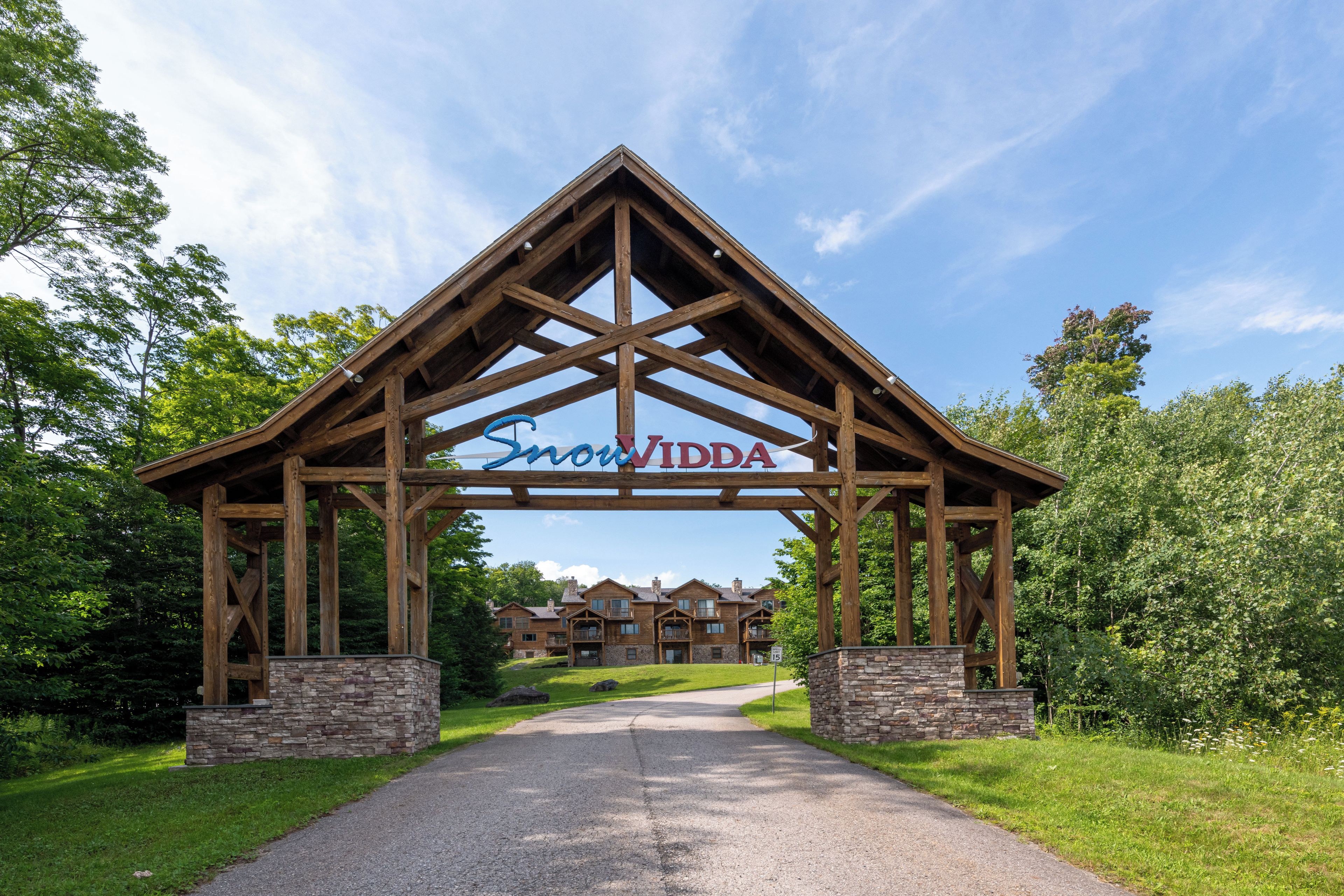 Une arche en bois surmontée de l’inscription « Snowy Ridge », au-dessus d’une allée menant à un bâtiment doté de nombreuses fenêtres et d’un socle en pierre.