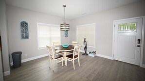 A dining area with a round table, four chairs, a chandelier, and a door with a window. - Seaglass Cottages (calabash)