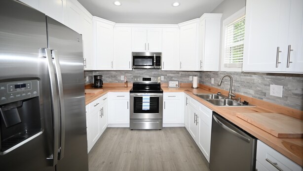 A modern kitchen with white cabinets, stainless steel appliances, a wooden countertop, and a built-in oven. - Seaglass Cottages (calabash)