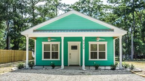 A small, single-story house with a green exterior and white trim, featuring a front porch and a number '9020' on the door. - Seaglass Cottages (calabash)