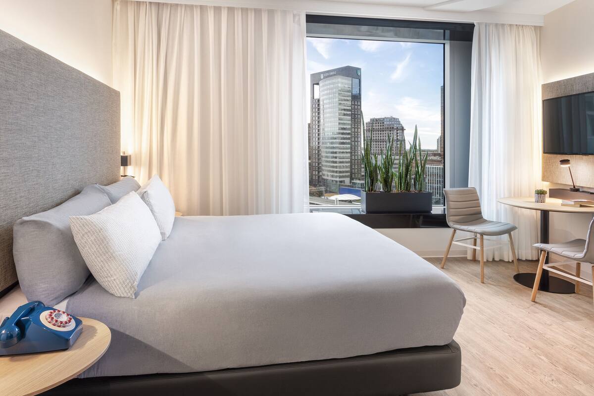 Quarto de hotel moderno com uma cama grande, uma escrivaninha, uma cadeira e uma televisão.
