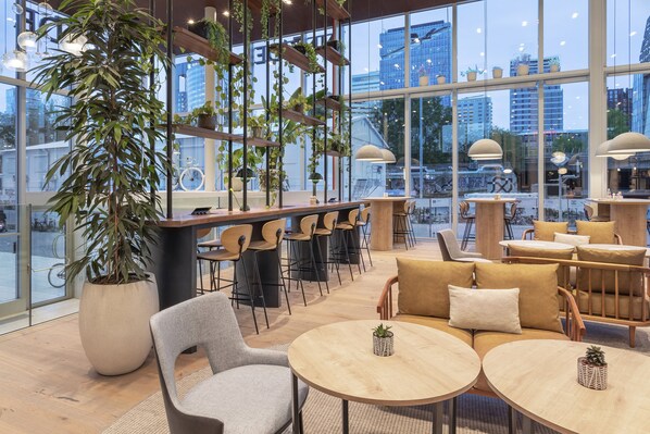 A modern cafe with large windows, wooden furniture, and indoor plants.