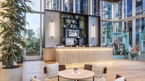 A modern reception area with a wooden reception desk, seating area with patterned cushions, and a large potted plant.
