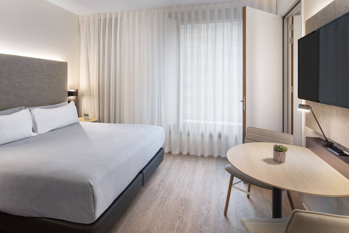 Quarto de hotel moderno com uma cama grande, uma mesa de jantar e uma televisão.