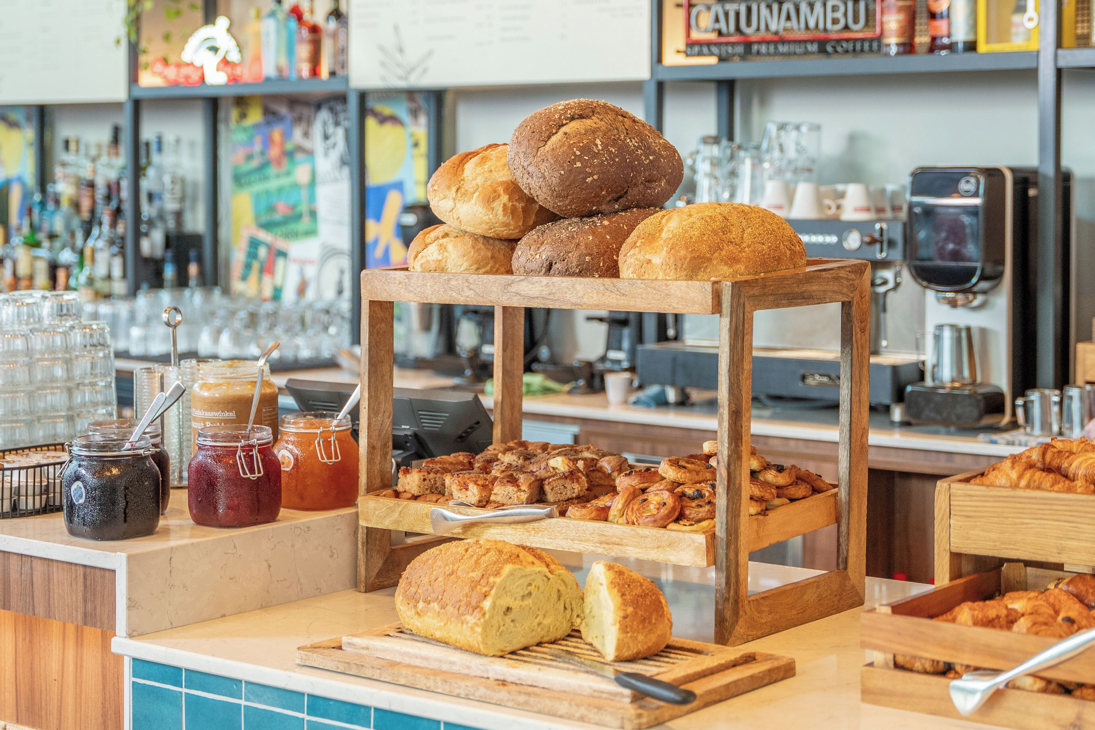 Eine Bäckerauslage mit verschiedenen Brotsorten und Backwaren, einer Kaffeemaschine sowie Gläsern mit Brotaufstrichen.