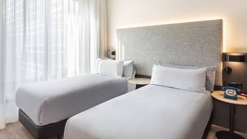 Una habitación de hotel con dos camas, una mesita de noche con lámpara y un teléfono.