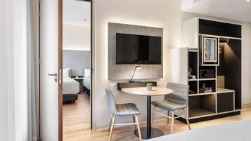 A modern hotel room with a bed, a TV mounted on the wall, a round table with two chairs, and a built-in wardrobe.