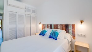 Une chambre à coucher avec un lit, des murs blancs, une tête de lit en bois et une table de chevet.