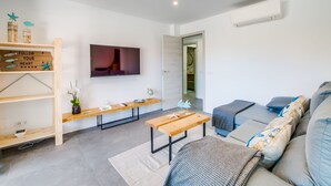 Un salon moderne doté d’un téléviseur à écran plat, d’une étagère en bois ornée d’objets décoratifs, d’un banc et d’un canapé avec des coussins.