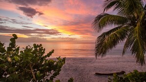 A beach with a sunset, palm trees, and a calm sea. - Pink Flamingo Beach House Private Beachfront Paradise with Pool Sleeps 12 (North Captiva)