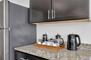 A kitchen with a granite countertop, a coffee maker, a kettle, and a French press. - Coffee Shops, Restaurants, Bars & Boutiques Just Steps Away • FREE Parking • Private Balcony Overlooking 12South (Nashville)