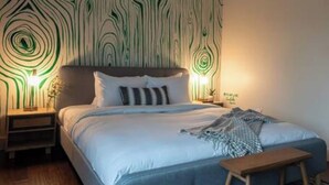 A bedroom with a patterned wallpaper, a bed with pillows, a bedside table with a lamp, and a wooden bench. - Coffee Shops, Restaurants, Bars, Salons and Boutiques, just steps away. (Nashville)