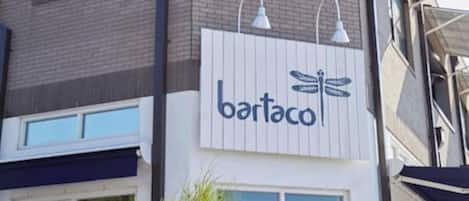 Un edificio con letrero de 'bartaco', con un diseño moderno que incluye techo plano y ventanas grandes.