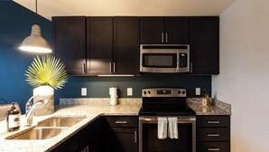 A modern kitchen with dark cabinets, a stainless steel microwave, a built-in oven, a granite countertop, and a pendant light. - Coffee Shops, Restaurants, Bars, Salons and Boutiques, just steps away. (Nashville)