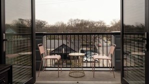 A balcony with two chairs and a small table, overlooking a parking area and a building with graffiti. - Coffee Shops, Restaurants, Bars, Salons and Boutiques, just steps away. (Nashville)