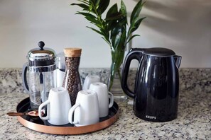 A coffee setup with a French press, a grinder, a pepper grinder, and several white cups on a copper tray.