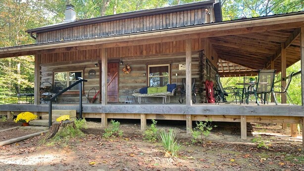 Un chalet rustique doté d’un porche abrité, d’un coin repas et d’un petit espace extérieur aménagé pour s’asseoir.