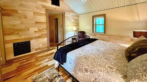 Une chambre avec un plancher en bois, un lit recouvert d’une couvre-lit à motifs floraux, un ventilateur de plafond, une fenêtre et une porte.
