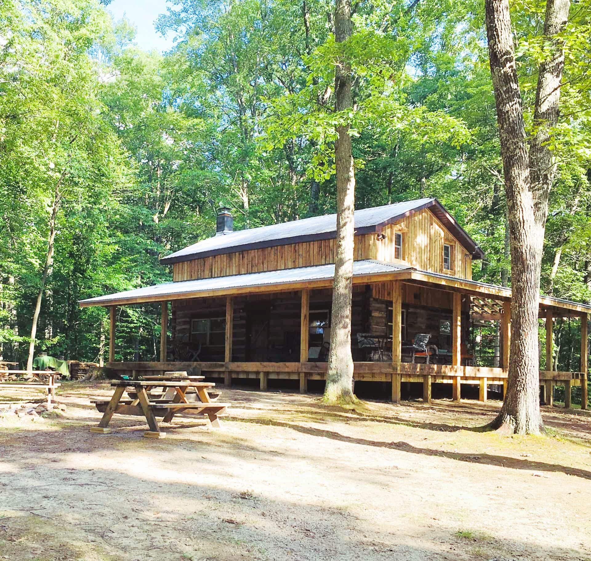A rustic cabin with a porch, surrounded by trees.