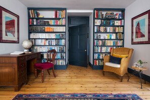 A room with wooden flooring, a desk with a globe, a chair, and two bookshelves filled with books.