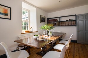 A dining room with a wooden table, white chairs, a vase with flowers, and a bookshelf with books and decorative items.