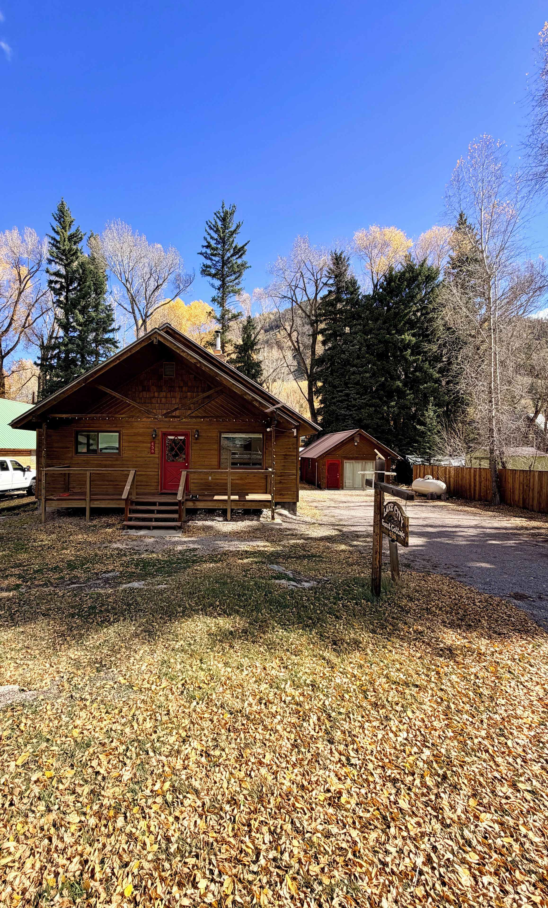 A rustic cabin with a red door, a bench outside, and a sign indicating it's a guest cottage.
