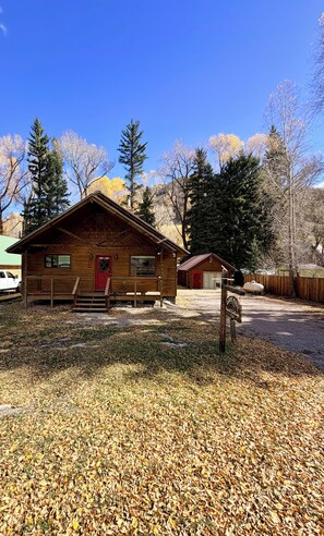 Un chalet rustique avec une porte rouge, un banc à l’extérieur et une pancarte indiquant qu’il s’agit d’une maison d’hôtes.