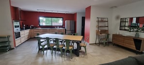 A modern kitchen with a dining area, featuring a large window, built-in appliances, and a wooden dining table with chairs.