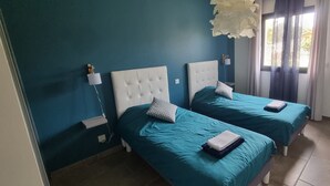 Et værelse med to senge, begge med hvide sengegærder og turkis sengetøj. Der er en hvid stikkontakt og en hvid lampe på væggen.