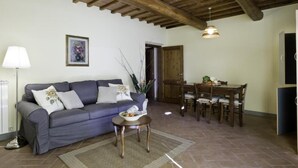 Una sala de estar con un sofá, una mesa de comedor con sillas, una lámpara y un cuadro en la pared.