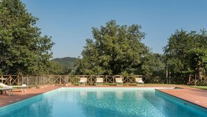 Una piscina rectangular con agua azul cristalina, rodeada por una terraza de madera y sillones de descanso.