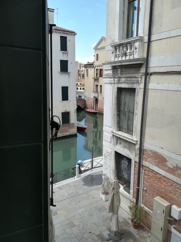 A narrow Venetian canal with buildings on either side, a small boat docked at the canal's edge, and a potted plant on the ground.