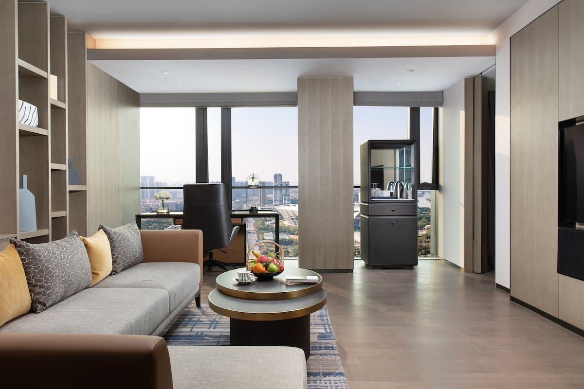 A modern living room with a sofa, coffee table, and a large TV. There is a view of a cityscape through large windows.