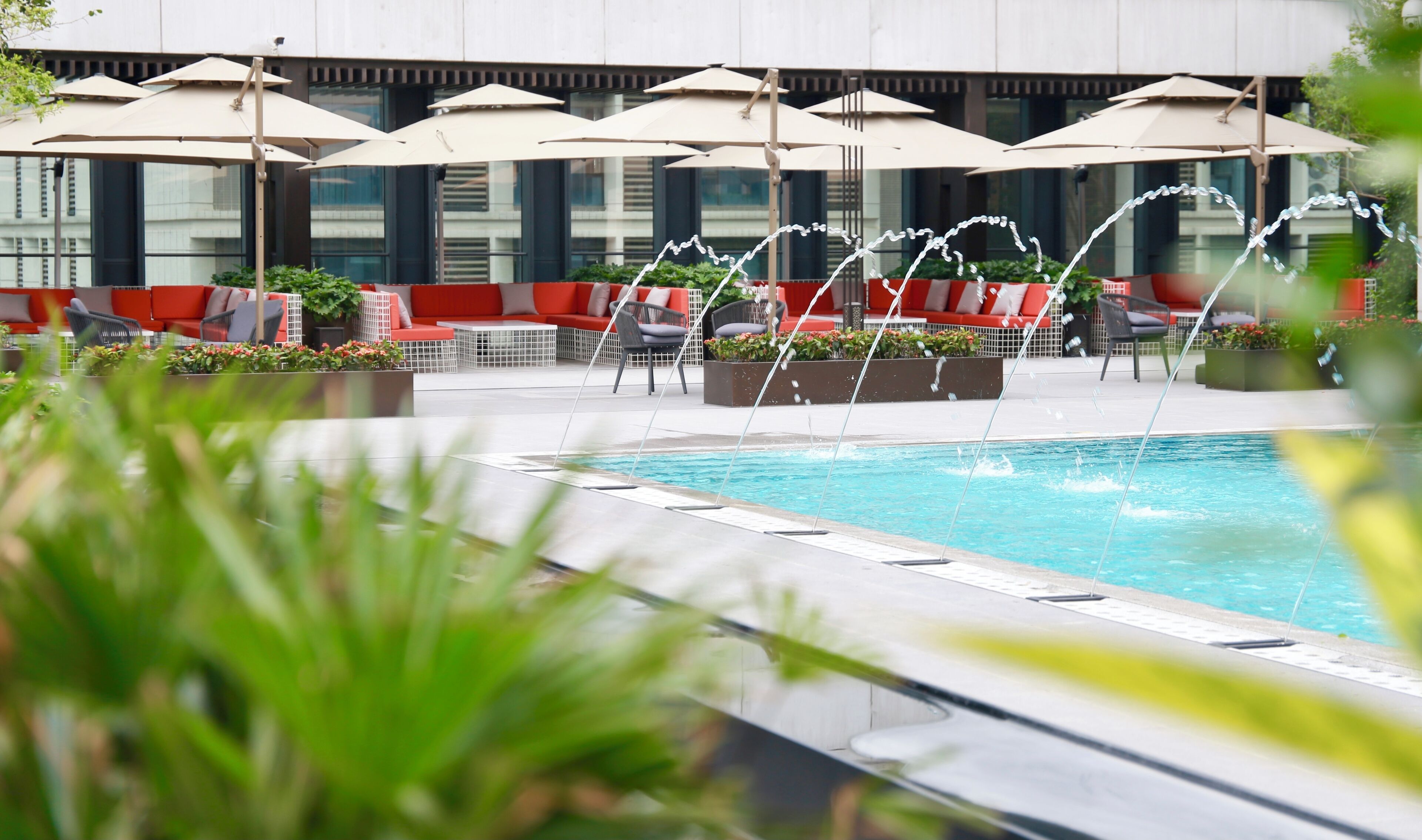A pool area with multiple lounge chairs and umbrellas, surrounded by a modern building with large windows.