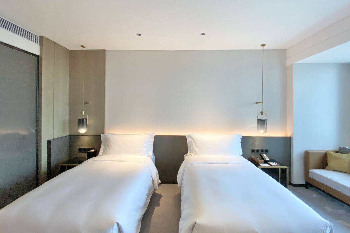A hotel room with two single beds, a nightstand with a phone, and a sofa.