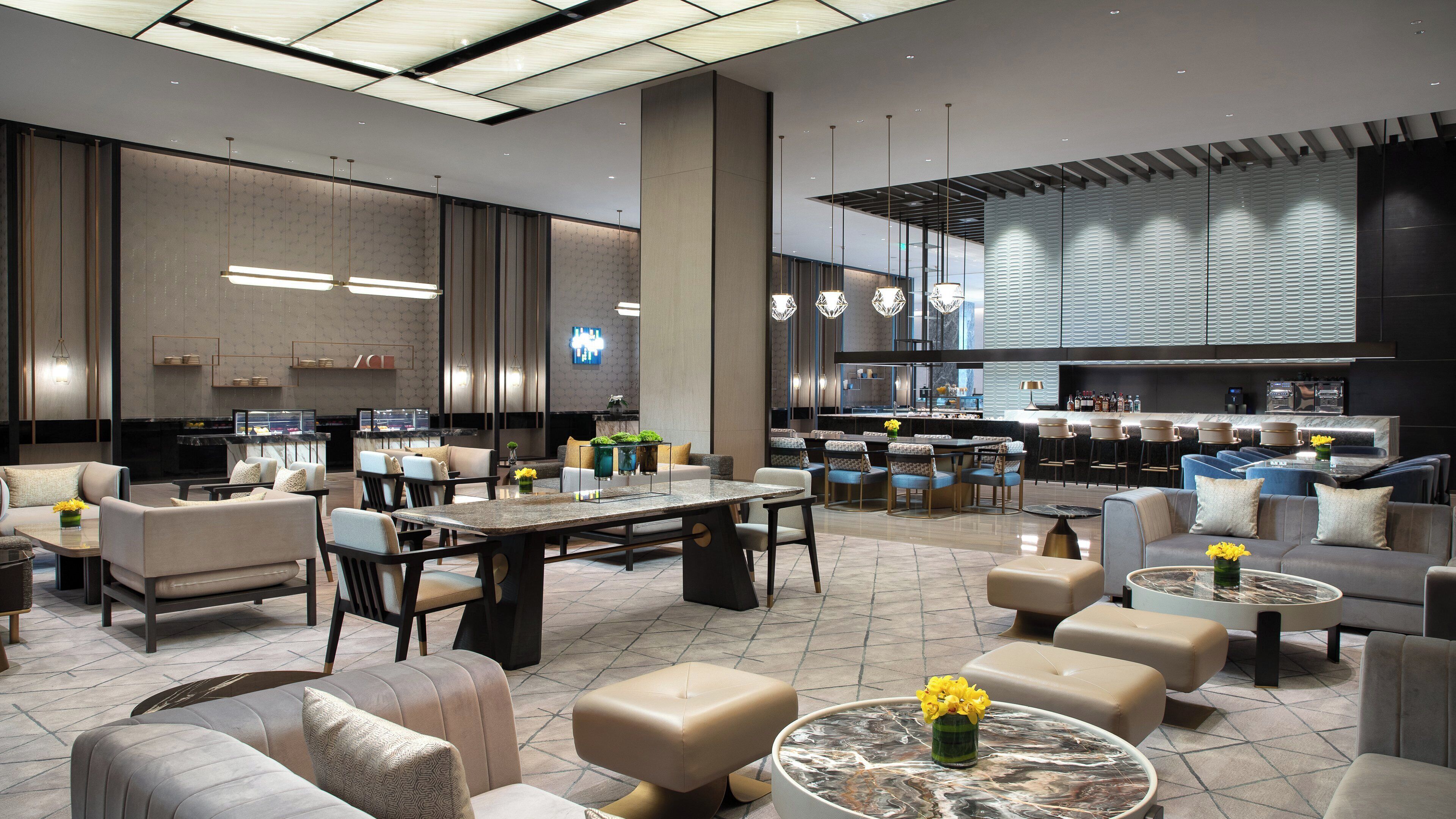 Un hall d’hôtel moderne comprenant un espace repas, des coins salon et un bar.