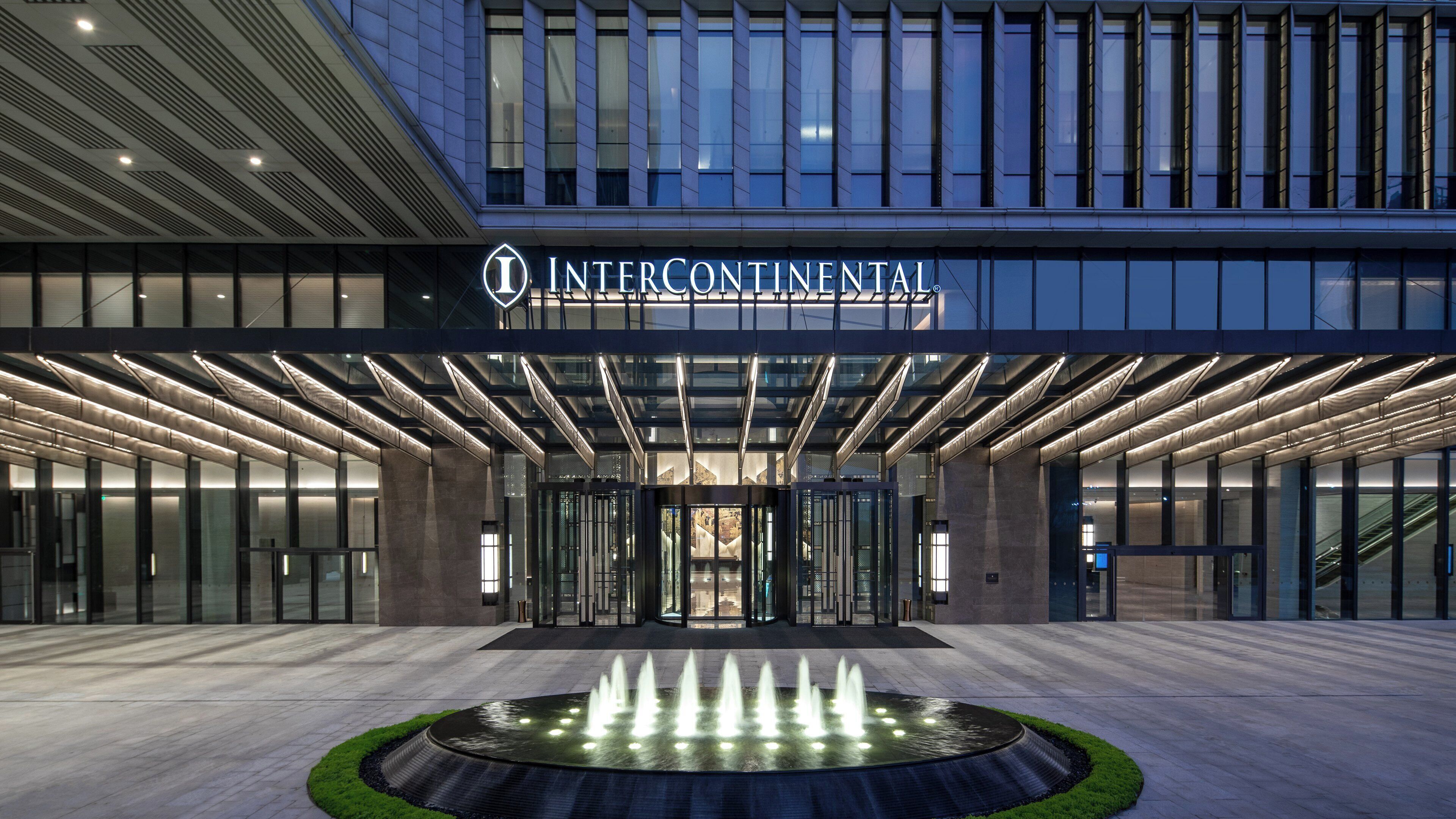 A modern hotel entrance with a glass facade, a central fountain, and a sign reading 'INTERCONTINENTAL'.