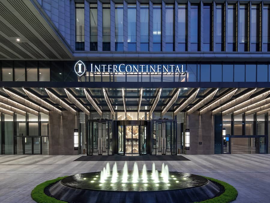 Une entrée d’hôtel moderne avec une façade en verre, une fontaine centrale et une enseigne indiquant « INTERCONTINENTAL ».