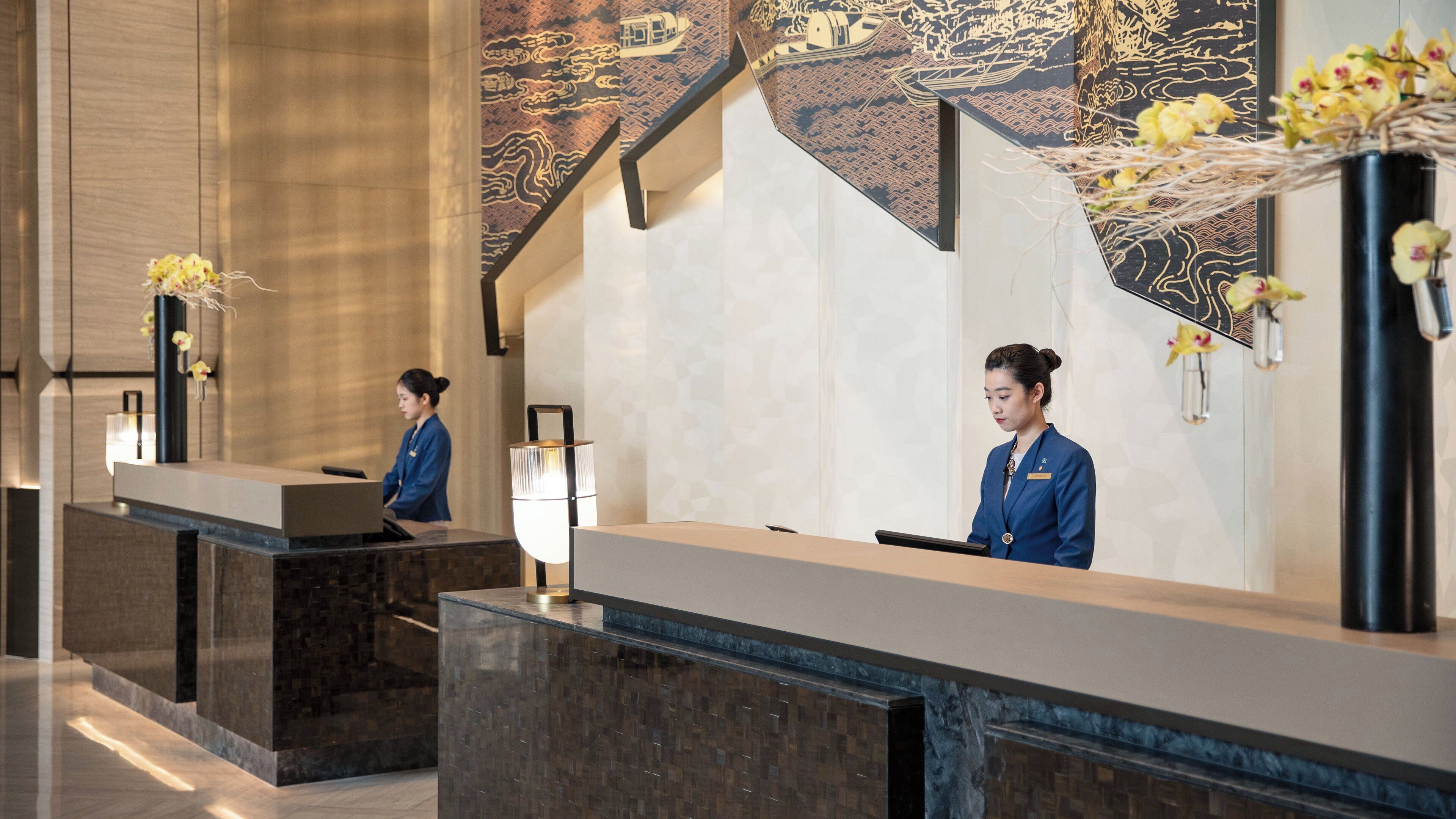 A reception desk with a modern design, a large vase with flowers, and a decorative wall with traditional patterns.