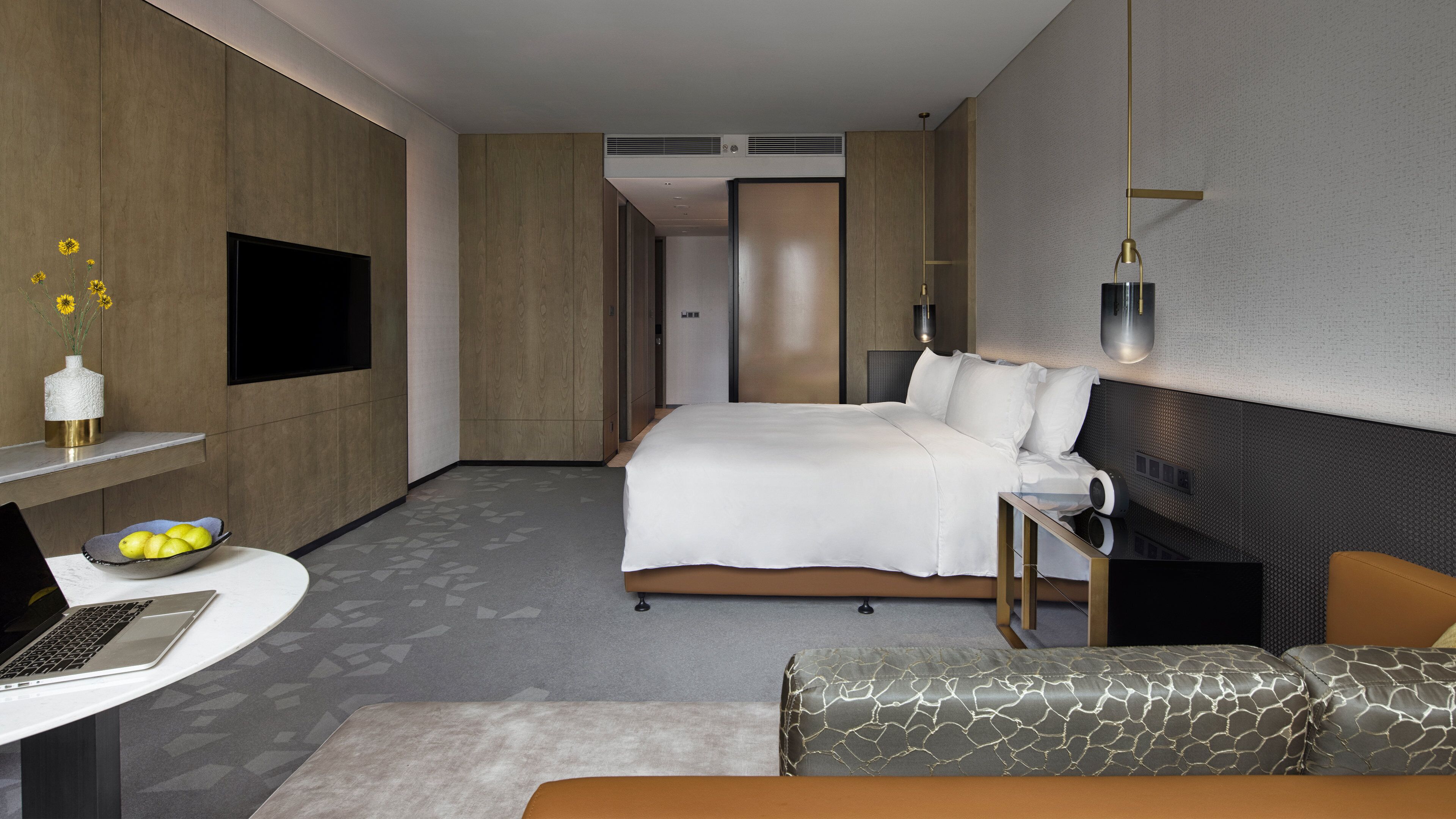 Una habitación de hotel moderna con cama, escritorio con computadora portátil, mesita de noche y sofá.