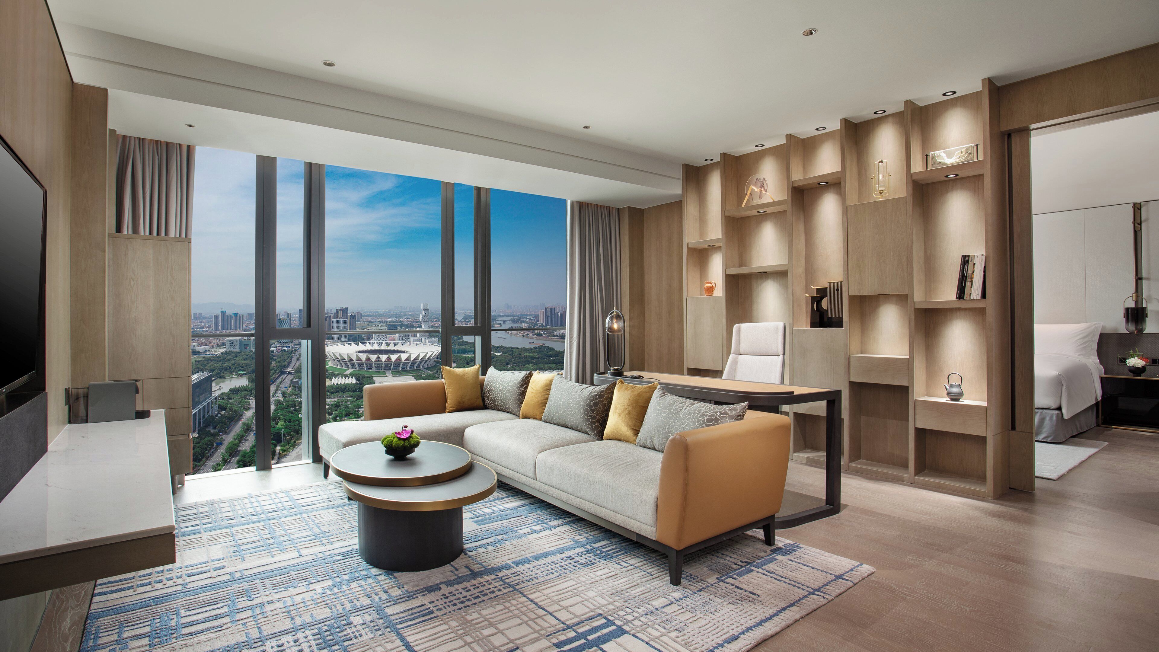 A modern living room with a large sofa, a coffee table, and a view of a cityscape through large windows.