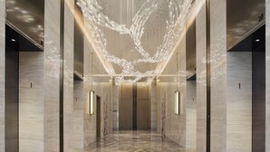 Un hall d’entrée moderne avec un sol en marbre poli, une installation lumineuse centrale et une conception symétrique, avec des ascenseurs de part et d’autre.