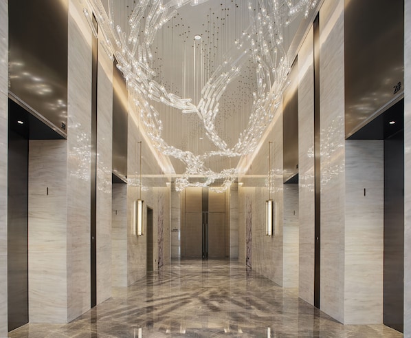 A modern lobby with a reflective marble floor, a central light installation, and a symmetrical design with elevators on either side.