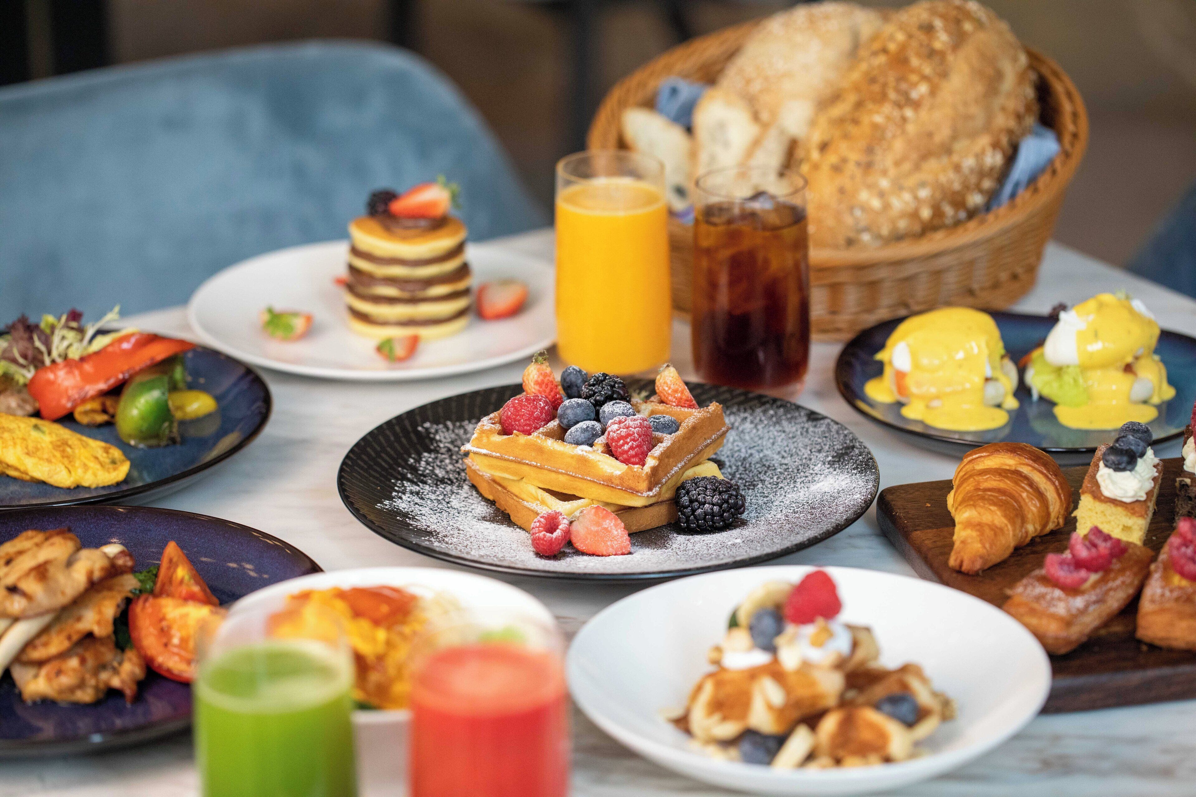 A breakfast buffet with various dishes including pancakes, waffles, and pastries, along with fresh fruits and beverages.