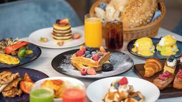 A breakfast buffet with various dishes including pancakes, waffles, and pastries, along with fresh fruits and beverages.